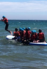 Our Charities - group of kids on sitting on top of a surfboard